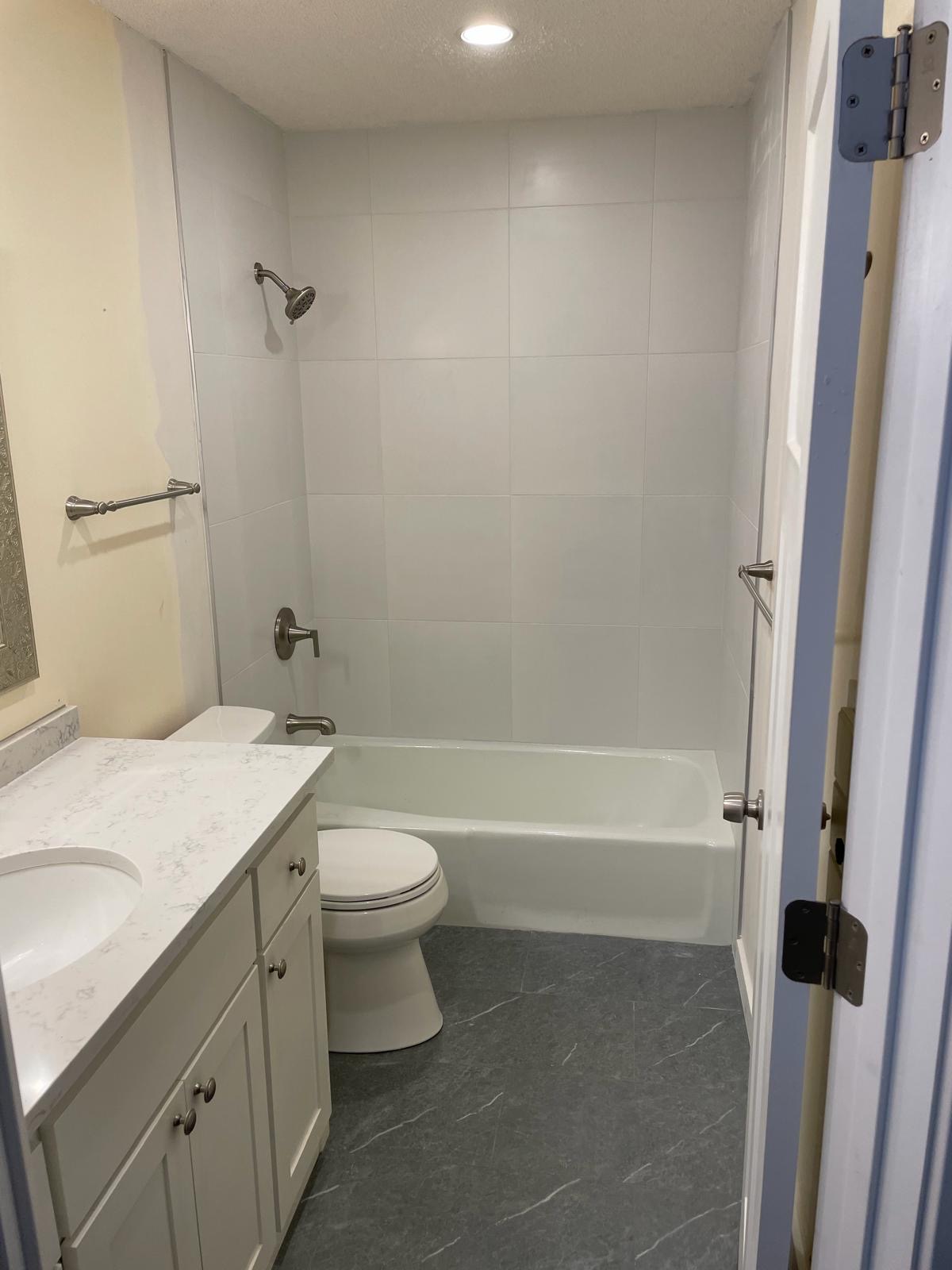 Finished bathroom with large-format white tile surround and new flooring